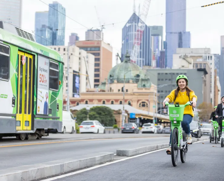 People riding bikes and scooters in the bike lane, next to a road with a tram in the city.