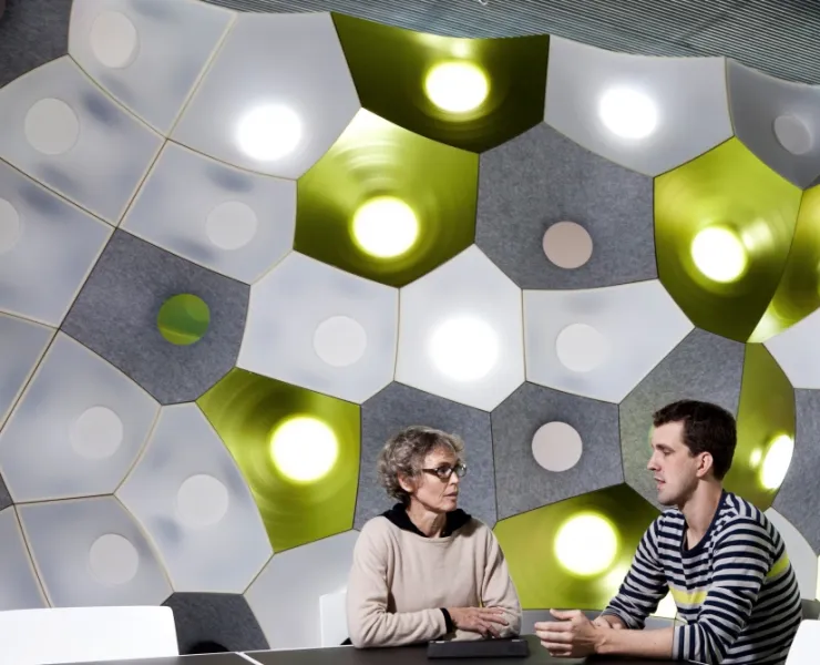 Two people sitting at a table with a wall of geometric patterns and lights