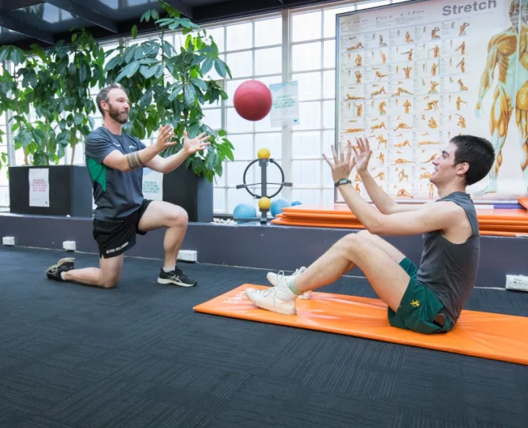 Trainer throwing ball to man sitting on mat at Melbourne City Baths gym