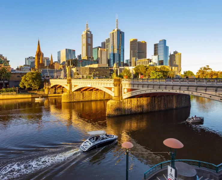 A boat driving down Yarra River with a bridge and the CBD skyline in the distance. 