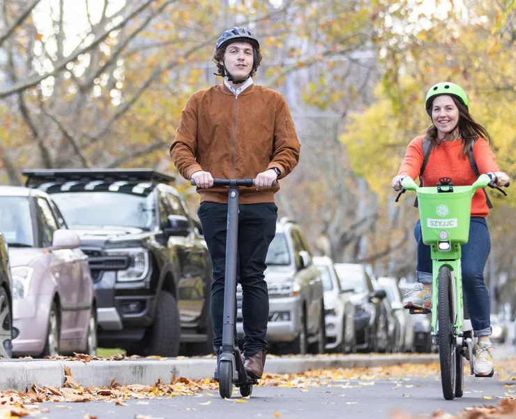 A person riding a private e-scooter alongside a cyclist on a hired e-bike.