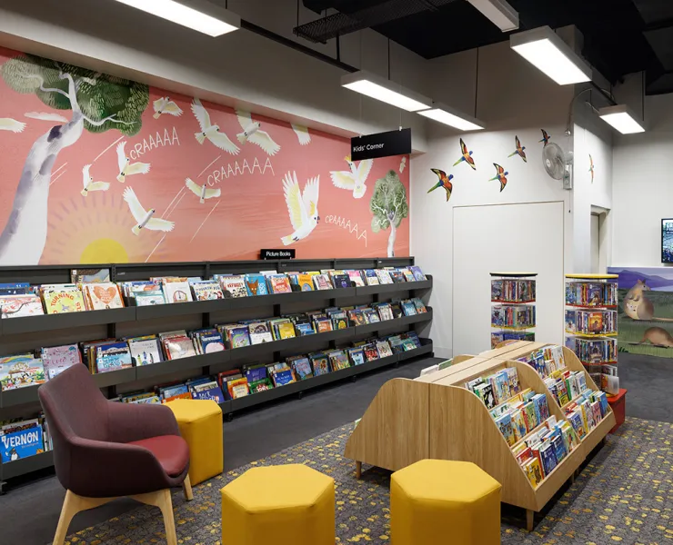A children's library space with low bookshelves, chairs and murals of flying birds decorating the walls. 