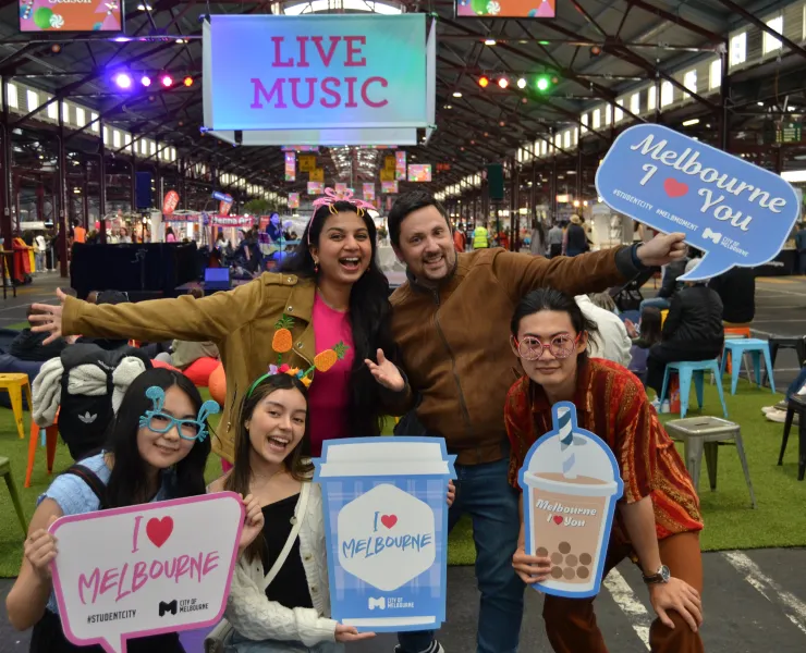 A group of people with 'I love Melbourne' signs posing for the camera inside an indoor marketplace