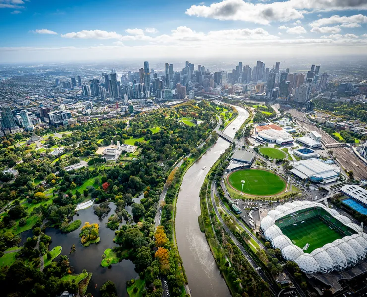 Aerial view of central Melbourne showing the CBD, with arenas and stadiums in the sports precinct and the botanical gardens on either side of the Yarra River.