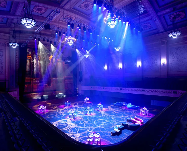 Interior of town hall with grand organ in background and multiple tables and couches all lit by dramatic purple-blue lighting.