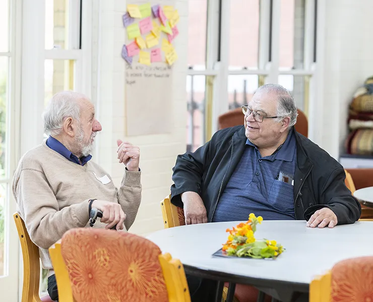 Two older men sitting at a table indoors talking.