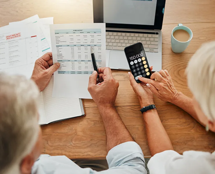 two older people studying a spreadsheet with a laptop and calculator