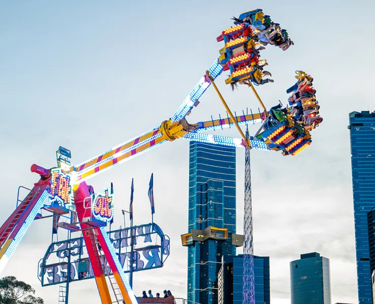 A carnival ride with people lifted up high, against a backdrop of the sky and CBD high-rise buildings.