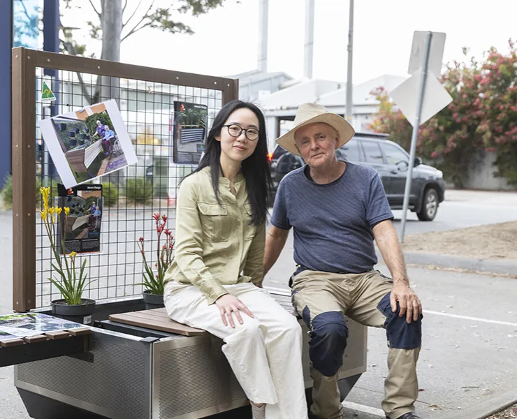Woman and man sitting on metal box looking towards camera.