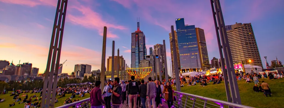 People on a boardwalk, with the city and sunset in the distance