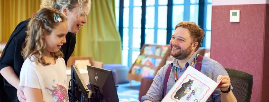 Mother and child borrowing books from smiling library staff