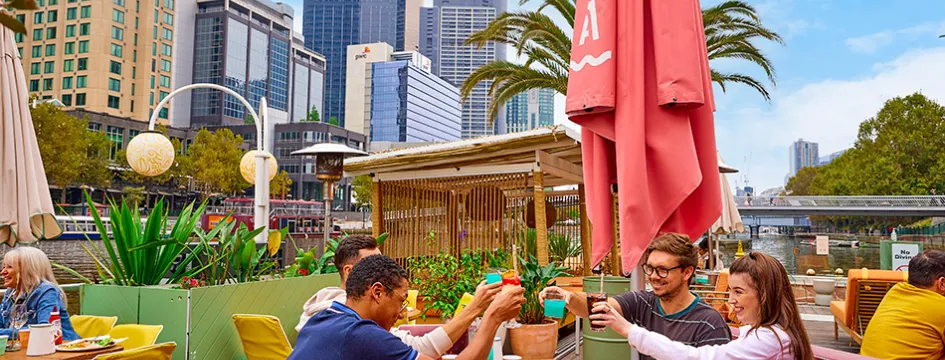 Group of people dining at an outdoor bar by the river.