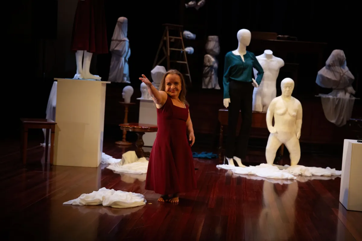 Performance with a woman in red dress reaching out and statues in the background