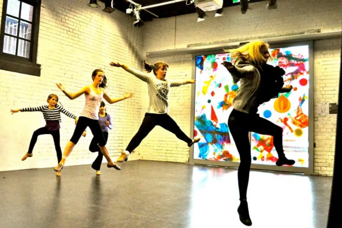 Four young people jumping while dancing in a room with white walls