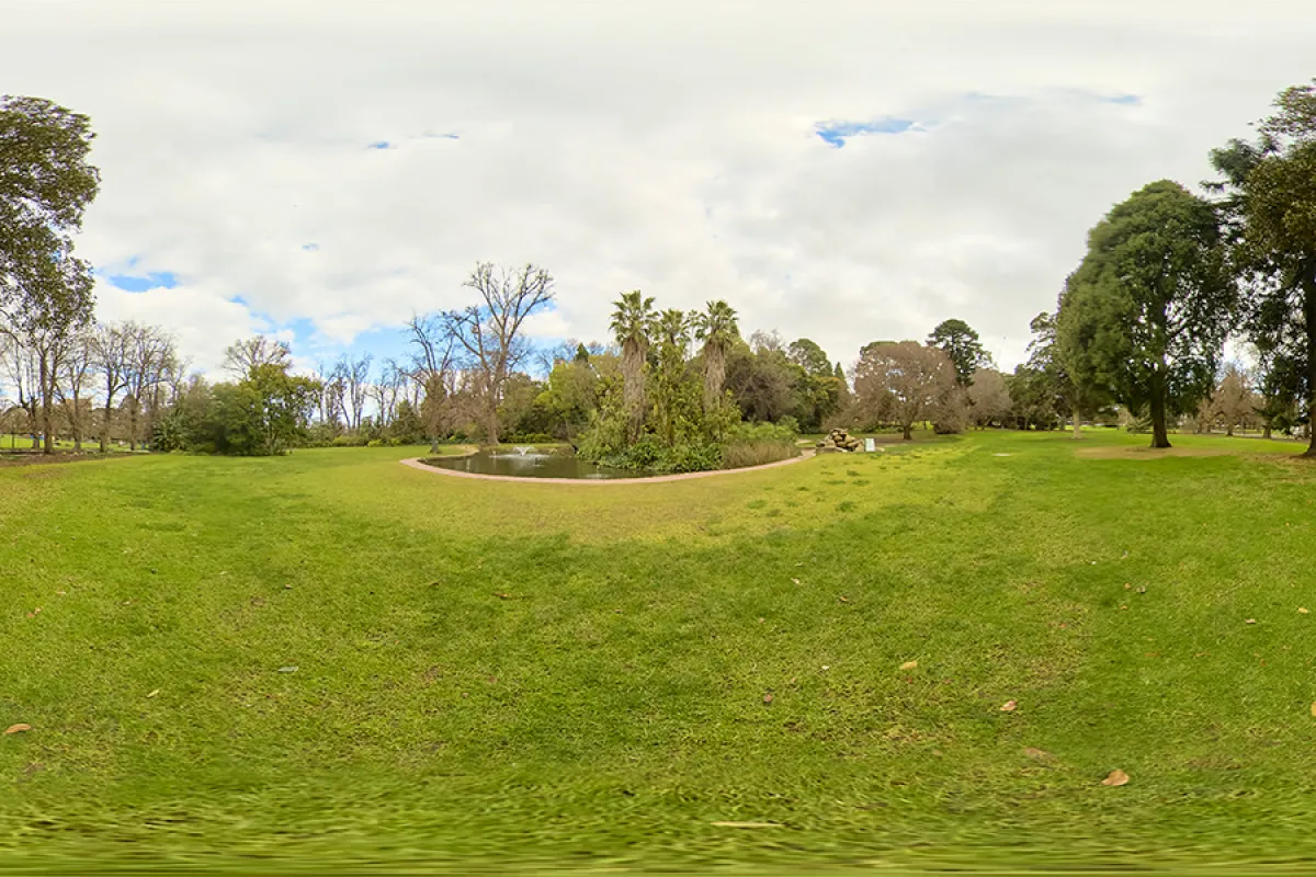 360-degree view of an expansive lawn area and trees around a pond with small fountain.