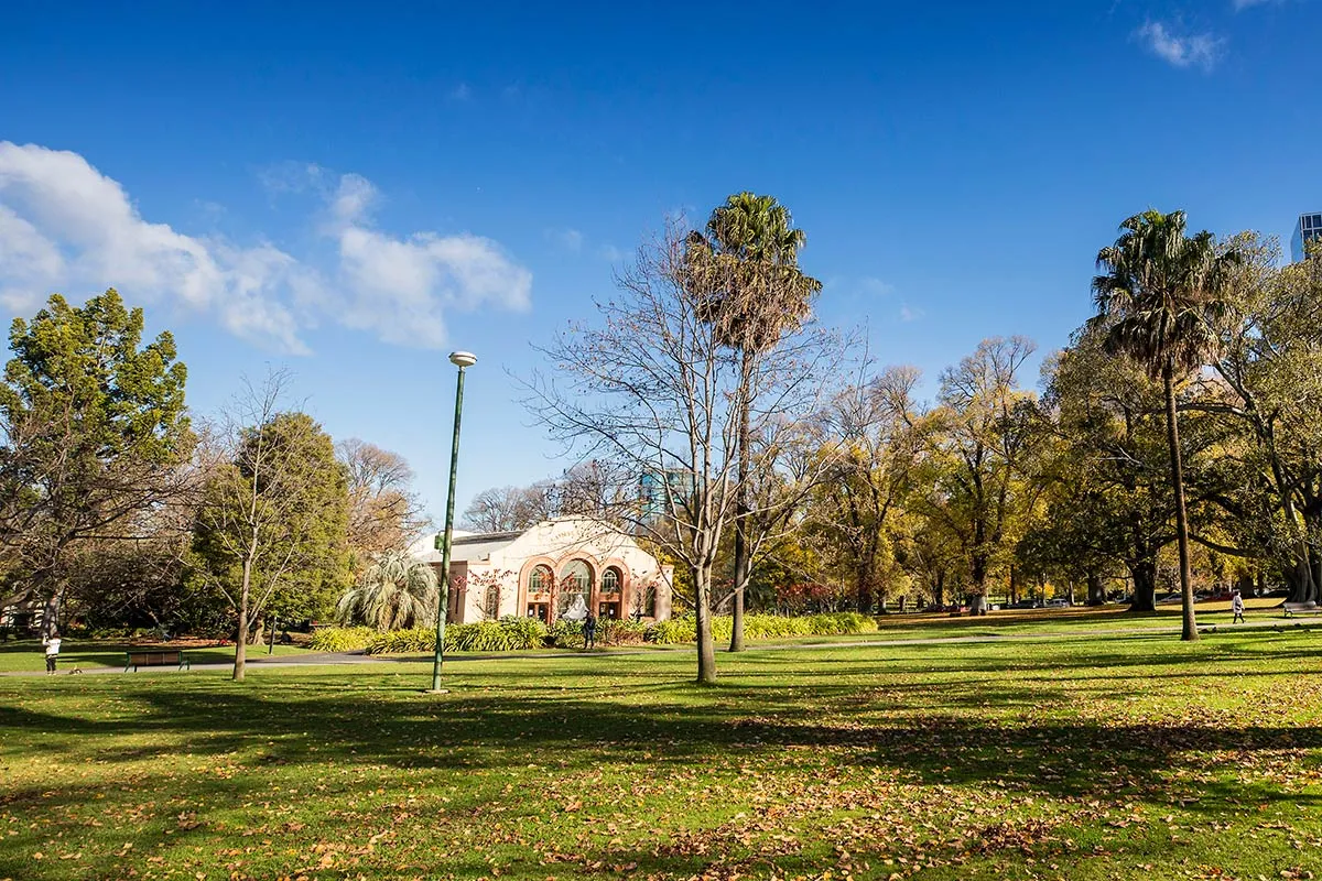 Trees in a park with a cream coloured conservatorium in distance
