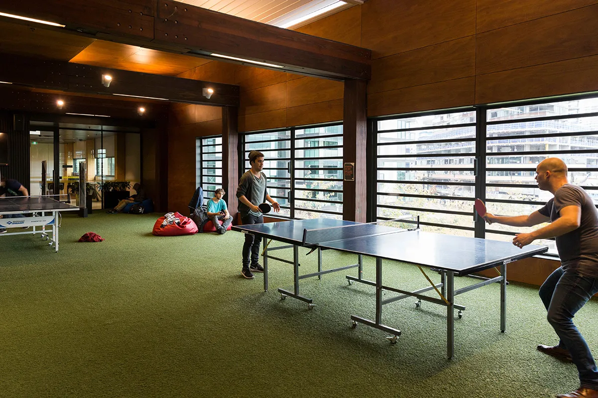 People playing table tennis in an indoor space with green floor.