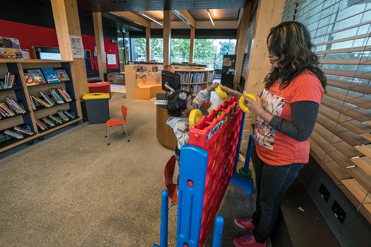 A woman and child playing with large four-in-a-row game in a library.