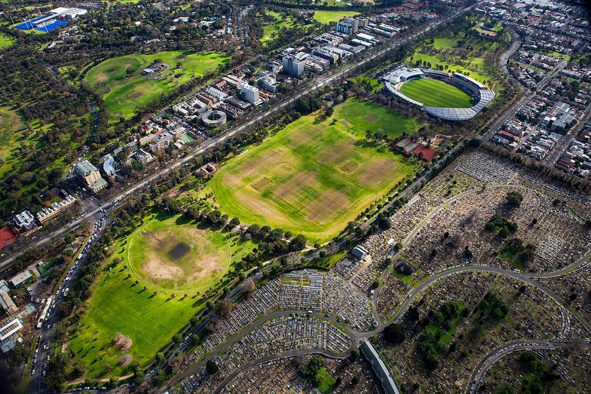 A birds-eye view of parkland, sporting grounds and a straight road with houses