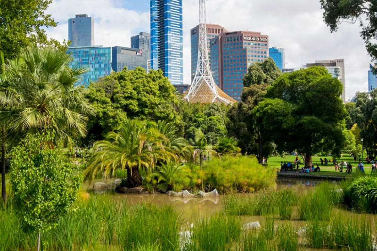 A child running in a park in front of a pond and city buildings