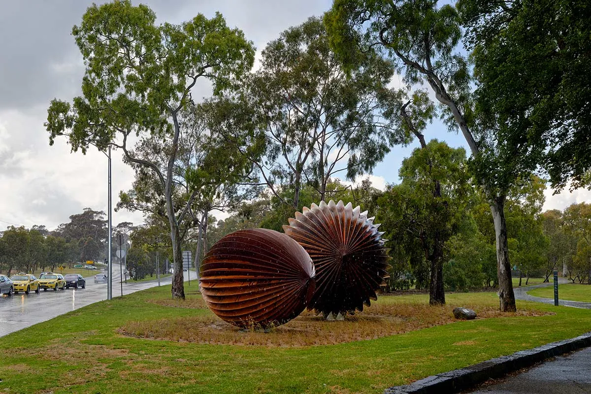 Two round brass sculptures on a grass media strip beside a road