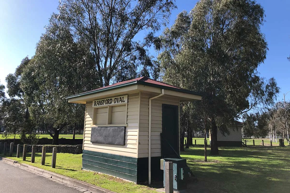 A small wooden building in beige and green with sign saying Ransford Oval