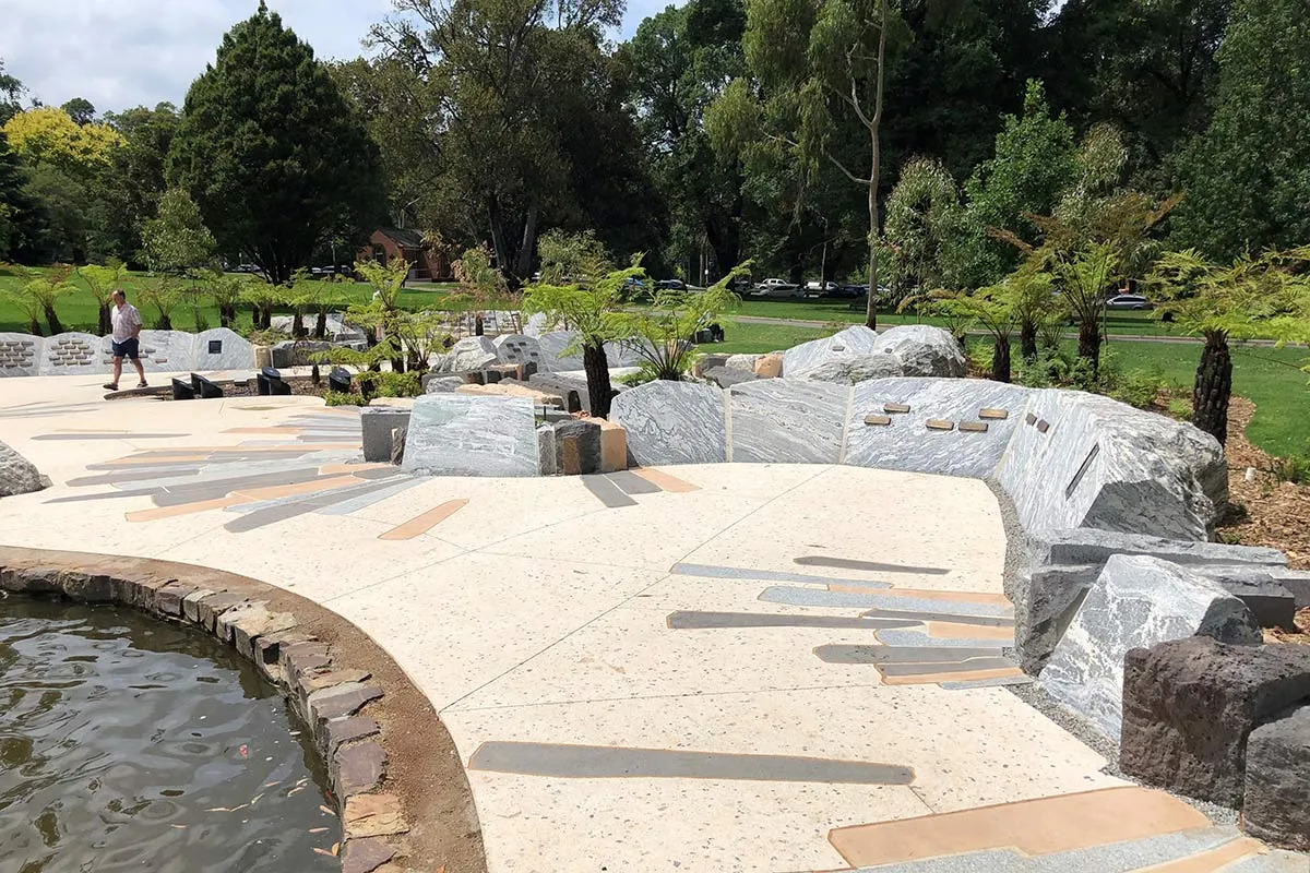 Stone memorial and benches around a paved pond