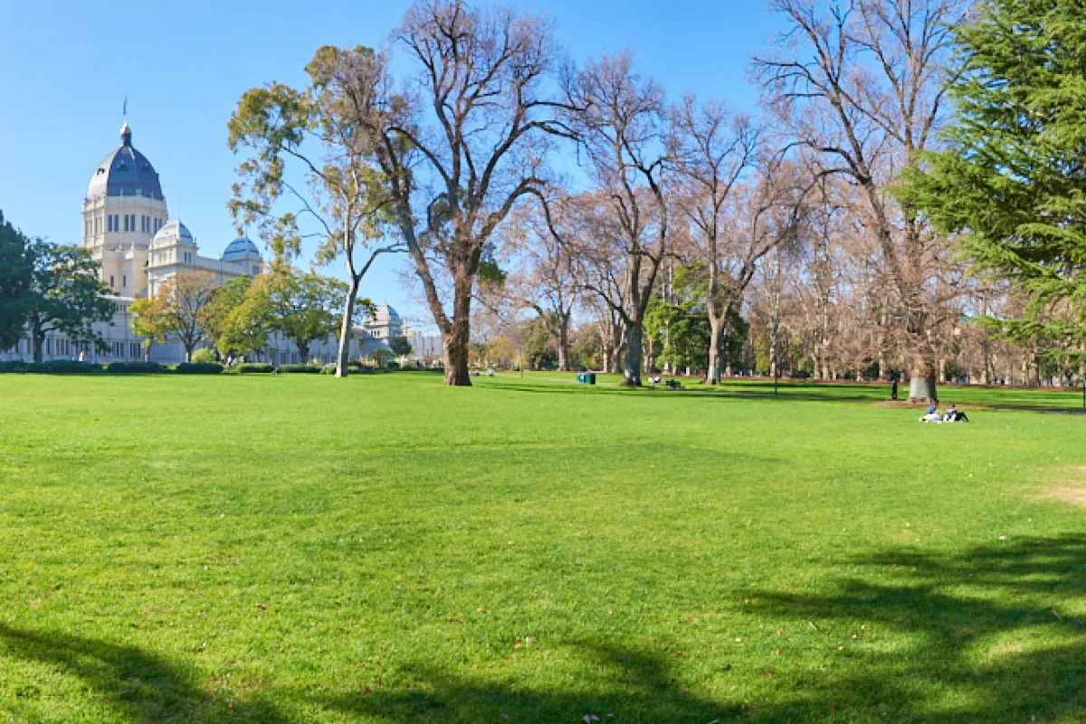 Wide expanse of lawn with trees in the middle distance and Exhibition Building seen in the background.