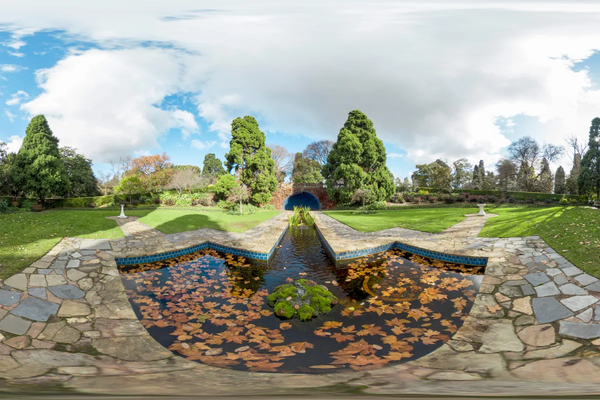 A distorted 360-degree view of a symmetrical water feature surrounded by paving and lawns. Paths lead to an archway flanked by large trees. 