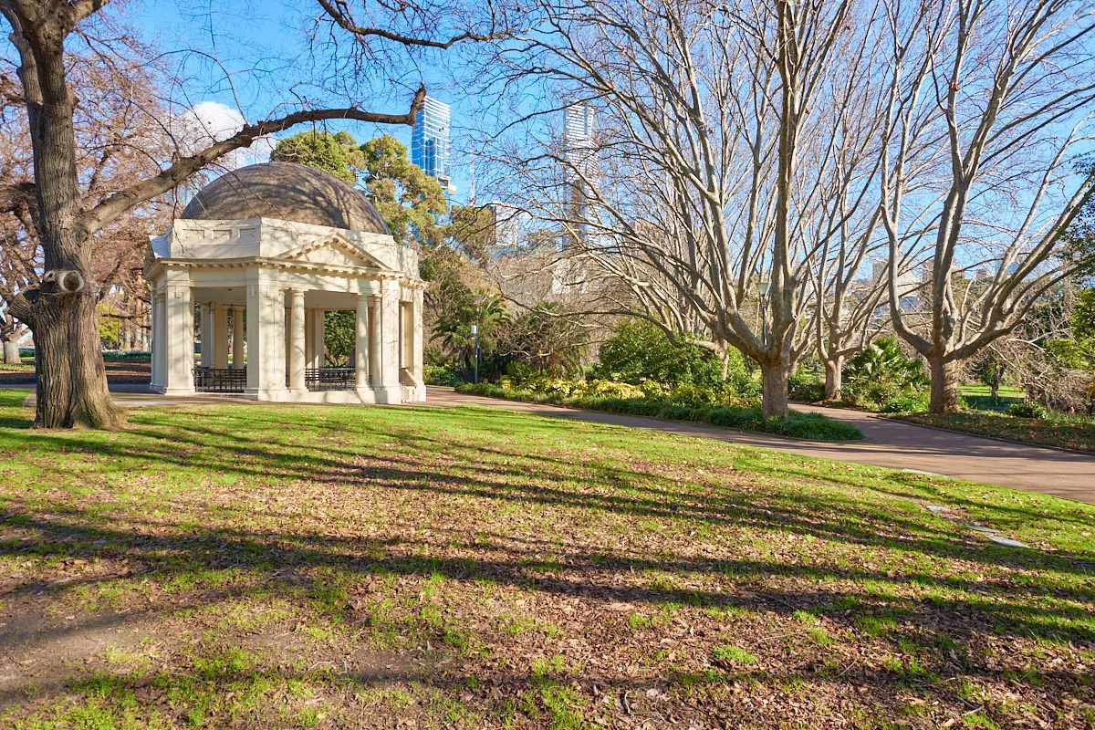 A lawn area featuring a rotunda with a domed roof and decorative columns, with footpaths, garden beds and large trees nearby.